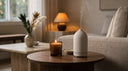 Appellation Stone Luna Diffuser emitting a gentle mist next to a glowing dark brown glass candle on a round walnut side table. 