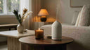 A lit candle beside an Appellation essential oil diffuser, comparing the two ways to scent a home.